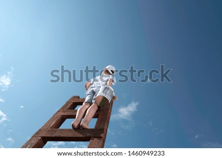 Cute little boy in baseball cap trying to paint the sky with a tassel ,climbing up the stairs to very height