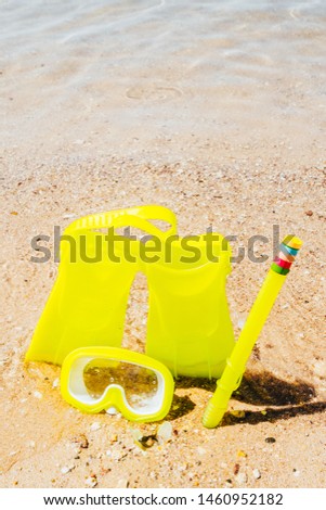 yellow swimming flippers with mask and tube on sand beach by the clear sea