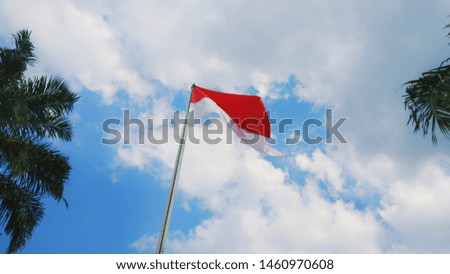 Indonesian red and white flag fluttering on a pole with a blue and cloudy sky background