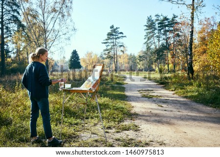 Portrait of drawing woman in autumn forest. Cheerful lady on the plein air, side view