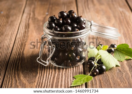 Fresh ripe black currant berry in a glass jar on a wooden background. Horizontal frame.