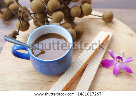 Milk coffee, wafer, longan fruit, and orchid on wooden plate, selective focused picture of light morning meal or breakfast. Wafer and coffee goes very well together for afternoon meeting break supper
