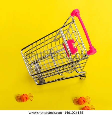 A miniature metal chrome trolley from a supermarket with a red handle, stands on a yellow background with Pink glass candy.