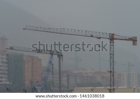 Rain in summer day in Basque country near Bilbao city in Las Arenas, Getxo. Cranes on the construction site and buildings in the fog. Close up photography