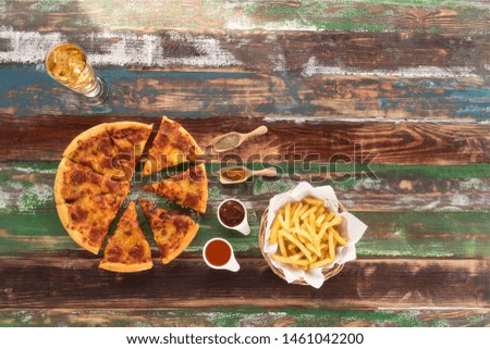 Delicious fresh Italian pizza and crispy french fries served on rustic wood table, with ketch up,chili sauce,  ingredients and drink