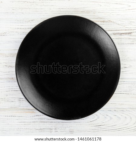 Black round plate on wooden background, top view, copy space.