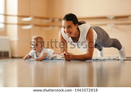 Athletic mother exercising in plank position while being with her baby on sports training. Copy space.  Royalty-Free Stock Photo #1461072818