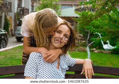Daughter and mother on the street in the summer. Teen girl hugs mother who is sitting on a bench. Relationship, parent-child relationship concept.