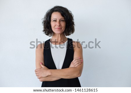 Cheerful middle aged woman with curly hair. Portrait of attractive brunette woman standing with crossed arms and smiling at camera isolated on grey background. Emotion concept
