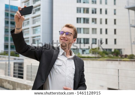 Smiling satisfied businessman taking selfie for profile. Young man in office suit and eyeglasses using smartphone camera for self portrait. Photography concept