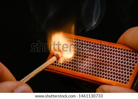 Man's fingers lighting a match, rubbing against the matchbox, setting fire to friction. On a black background. Matches and fire.