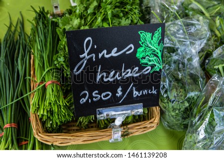 Organic produce sold at farmer's market. A close up view of a French sign showing fine herbs for sale on a market stall, bunches and bags of salad greens are seen behind, during a harvest fair.