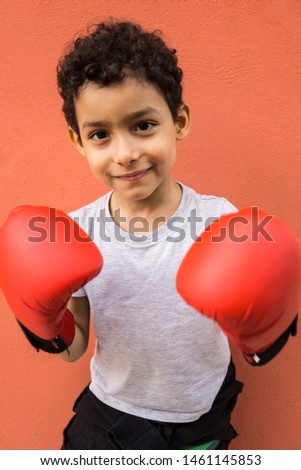Child with red boxing gloves. Red wall background. Gray pullover, curly hair Royalty-Free Stock Photo #1461145853