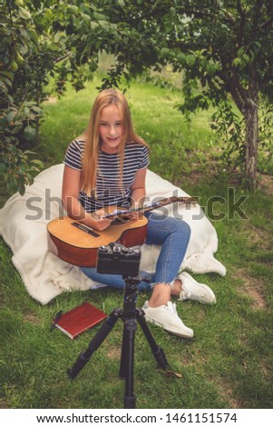 Teen girl shoots a blog on music and learning online guitar playing in nature in front of the camera, the idea of youth hobbies