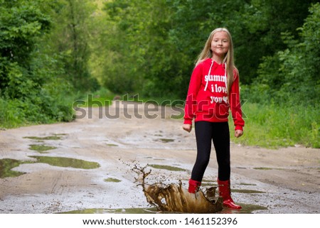 Young girl in red rubber boots walking in puddles