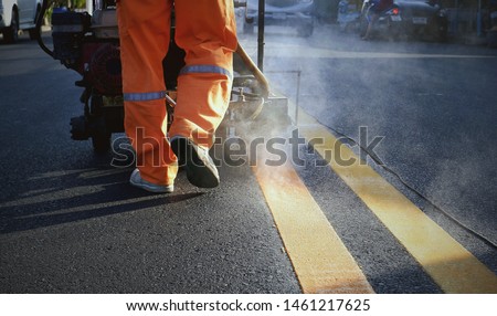 Low section of Road Worker using Thermoplastic Spray Marking Machine to Painting Yellow lines on Asphalt road Surface in evening time  Royalty-Free Stock Photo #1461217625