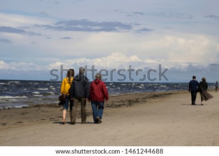 Promenade. Three people and couple walk by sea coast or ocean edge along the sandy beach. Background landscape photo on the subject of travel, tourism, leisure, family and active lifestyle.
