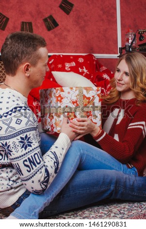 Happy young people give each other gifts by the fireplace near the Christmas tree. Lovers couple are full of anticipation for new year