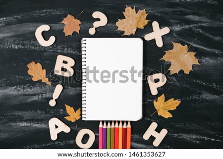 Back to school concept. School equipment with notebook, colored pencils, dried maple leaves on black table background. Flat lay, top view, copy space.