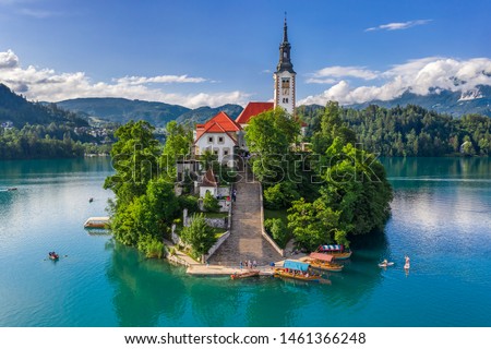 Bled, Slovenia - Aerial view of beautiful Pilgrimage Church of the Assumption of Maria on a small island at Lake Bled (Blejsko Jezero) and lots of Pletna boats on the lake at summer time with blue sky Royalty-Free Stock Photo #1461366248
