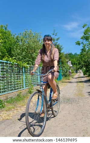 Attractive young woman in a summer dress riding a bicycle down a rural lane in summer sunshine