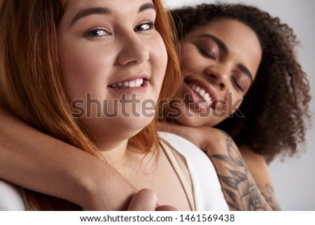 Close up of happy Caucasian woman and Afro American lady with tattoo on arm having rest together