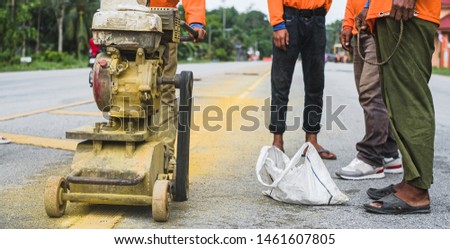 Worker using the thermoplastic spray marking machine to paint yellow line in road work construction.