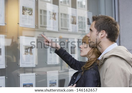 Side view of a young couple looking at window display at real estate office Royalty-Free Stock Photo #146162657