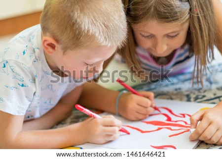 Brother and sister drawing on floor on paper. Preschool boy and girl play on floor with pencil and paper