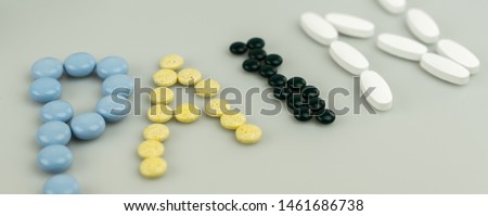 horizontal close up of the word pain written with different color prescription pills and painkillers