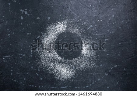 Circle of powdered sugar on a dark stone surface.Top view.