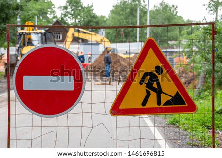 Road signs "travel is prohibited" and "road works" on a defocused background of workers and construction equipment