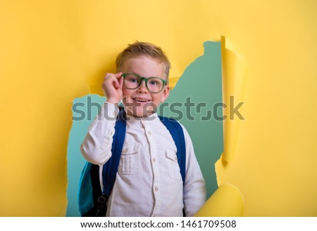 Children go back to school. Pupil of primary school with backpack and book breaking yellow paper wall. Beginning of lessons. First day of fall. Elementary student.