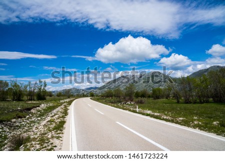 Montenegro, Curved asphalt road alongside green pastures with sheep herd animals and green mountains in rural countryside nature landscape with blue sky