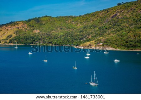 Yachts and catamarans in a quiet sea bay on a background of blue sea and island beach. Picture of idyllic sunny day in the tropics in high tourist season. Nai Harn and Ao Sane beach, Phuket, Thailand