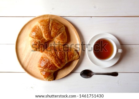 Cup of tea and wooden dish with croissants on white wooden background.


