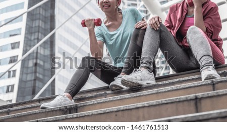 Couple friends sporty asian women are sitting lift dumbbells for exercises at city background. Half portrait concept, dramatic tone.