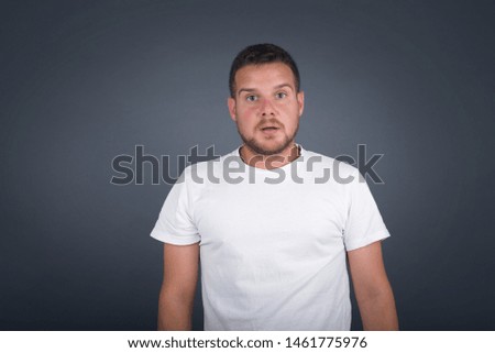 Emotional attractive male with opened mouth expresses great surprisment and frighteness, poses against white concrete background, stares at camera. Unexpected shocking news and human reaction.