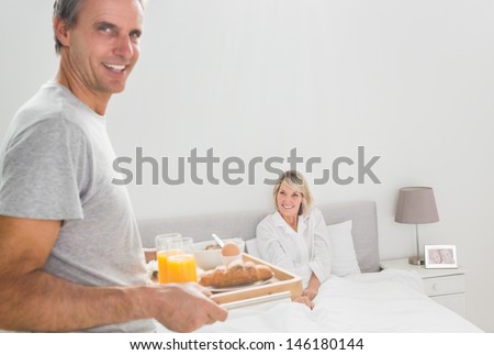 Cheerful man bringing breakfast in bed to his partner at home in bedroom