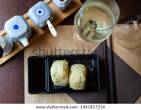 Top view of classic Japanese onigiri - rice triangles with nori and soy sauce on black plate served with glass of white wine

