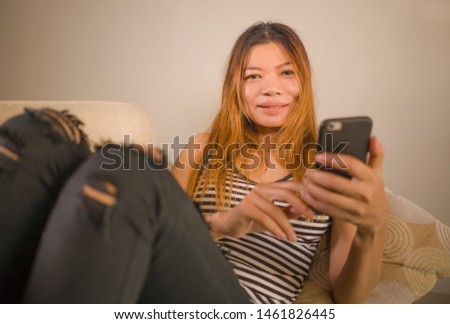lifestyle portrait of young attractive and relaxed 30s Asian Indonesian woman lying comfortable with mobile phone at home living room couch using internet social media or online dating app 
