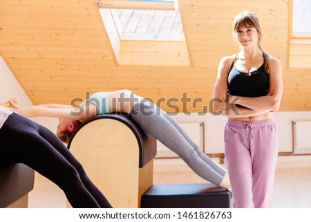Portrait of excited female pilates teacher posing over fitness equipment looking at camera, happy fitness instructor or coach in sportswear smiling making picture during training in studio.