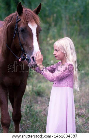 innocent blonde girl looking at the horse in forest. beautiful Caucasian girl with long blonde hair in a pink dress hugs a brown horse. innocent childhood concept. natural beauty. hipster style.
