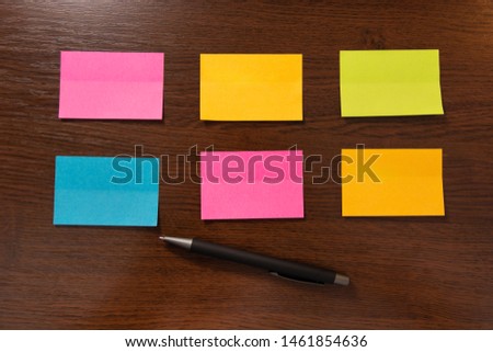 Six colorful sticky notes in two row and pen on brown wooden desk. Top view and space for text. Close up, selective focus
