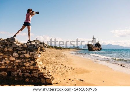 Tourism vacation and travel. Woman tourist on beach taking photo with camera, shipwreck in the background
