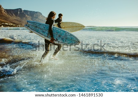 Two male surfers going for surfing in the sea. Two men carrying surfboards running in to the sea for surfing. Royalty-Free Stock Photo #1461891530