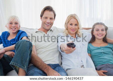 Parents posing with children and watching television sitting on a couch