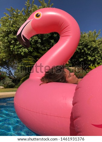 Young woman lying on a big pink flamingo in a swimming pool, eyes shut, asleep. Low angle view point
