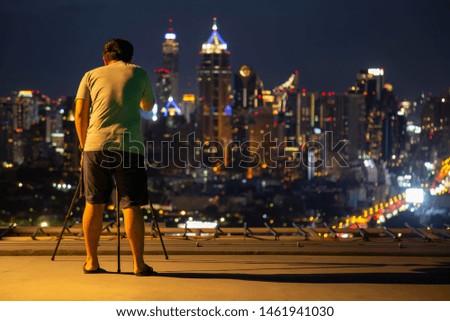 The photographer is taking a picture of the city on the rooftop. at Bangkok ,Thailand. The photographer stood on the deck and was photographing the beauty of the capital at night.