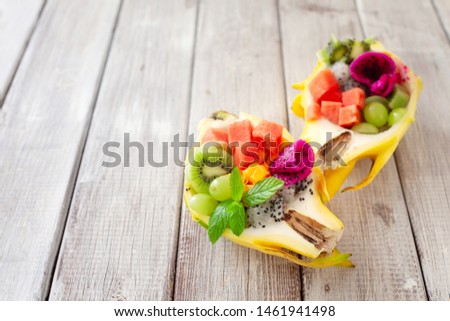 healthy fruit tropical salad served in half of yellow pitaya on wooden background, copy space